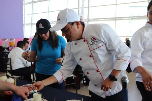 Coach supervisando una dinámica de integración de equipos de preparar comida en un auditorio con comensales presentes.