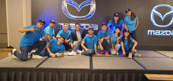 Equipo de trabajo en una dinámica de integración empresarial en una tarima con el isologo de Mazda al fondo.