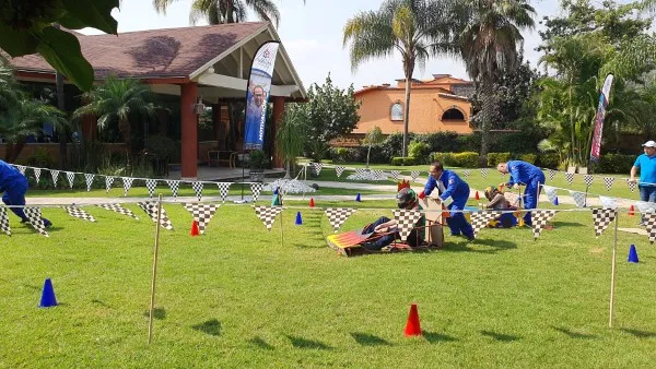 Persona empujando a otra en un carrito artesanal dentro de una pista improvisada en un espacio abierto y verde, se trata de una dinámica de integración de equipos.