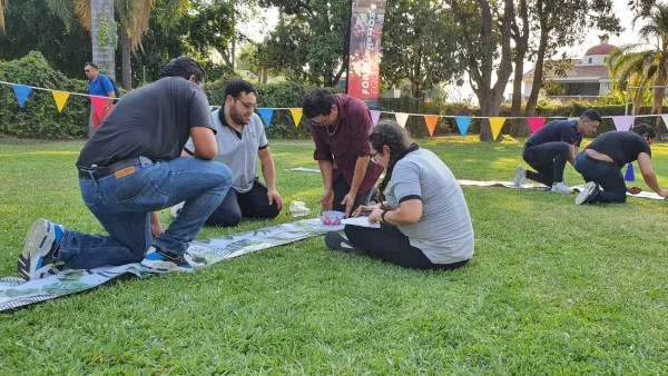 Grupo de personas realizando una dinámica en un parque al aire libre de motivación de equipos donde están creando una figura sobre el pasto.